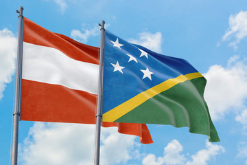 Solomon Islands and Austria flags waving in the wind against white cloudy blue sky together. Diplomacy concept, international relations.
