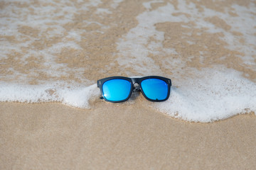 Blue fashion sun glasses on the sand with wave and beach