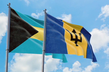 Barbados and Bahamas flags waving in the wind against white cloudy blue sky together. Diplomacy concept, international relations.
