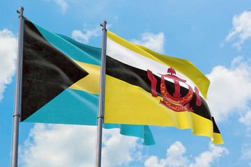 Brunei and Bahamas flags waving in the wind against white cloudy blue sky together. Diplomacy concept, international relations.