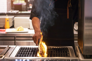 Chef cooked steak on grill with flames.