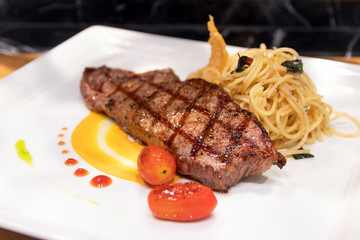 Medium grilled striploin beef steak with spaghetti olio a side dish served on white dish.