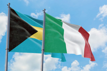 Italy and Bahamas flags waving in the wind against white cloudy blue sky together. Diplomacy concept, international relations.