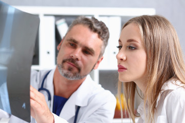 Mature male doctor hold in arm and look at xray photography discussing it with female patient portrait. Bone disease exam medic assistance cancer test healthy lifestyle hospital practice concept