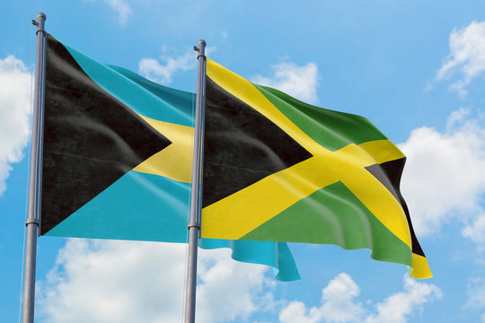 Jamaica and Bahamas flags waving in the wind against white cloudy blue sky together. Diplomacy concept, international relations.
