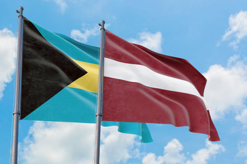 Latvia and Bahamas flags waving in the wind against white cloudy blue sky together. Diplomacy concept, international relations.