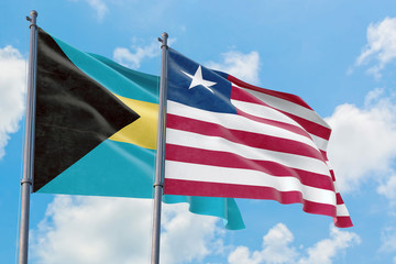 Liberia and Bahamas flags waving in the wind against white cloudy blue sky together. Diplomacy...