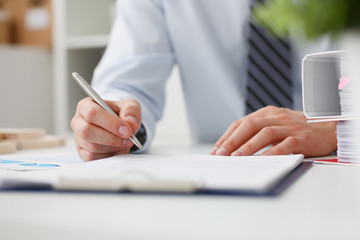 Male hand holding silver pen ready to make note in opened notebook sheet. Businessman in suit at...