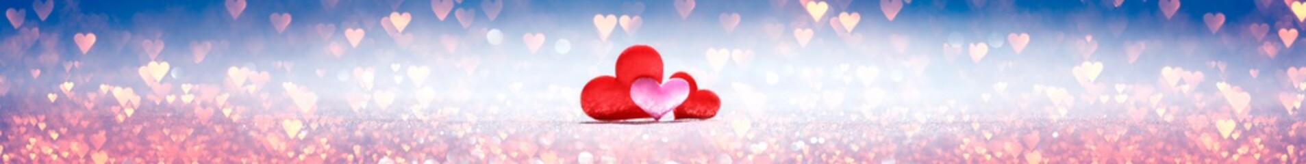 Obraz premium Three little red and pink hearts on background sparkling with a bokeh of pink and blue hearts. For love, romance, or Valentine's day.