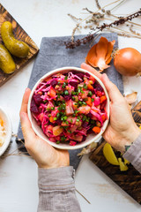 Vinegret or vinaigrette Russian red salad with cooked and pickled vegetables, peas, beetroot. Woman holds vegan healthy dietary food
