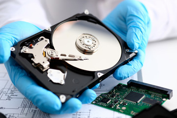A male repairman wearing blue gloves is holding a hard drive from computer or laptop in hands....