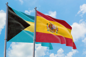 Spain and Bahamas flags waving in the wind against white cloudy blue sky together. Diplomacy concept, international relations.
