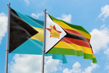 Zimbabwe and Bahamas flags waving in the wind against white cloudy blue sky together. Diplomacy concept, international relations.
