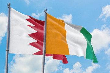 Cote D'Ivoire and Bahrain flags waving in the wind against white cloudy blue sky together....