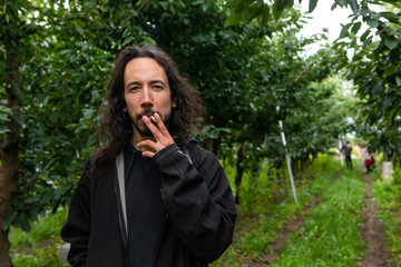 A young man smoking cigarettes in the cherry orchard. Professional cherry-picker smoking during his...