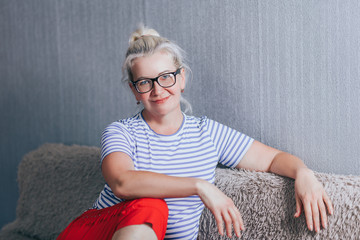 Smiling mature woman in black glasses, sitting on sofa at home. myopia.