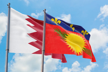 Guadeloupe and Bahrain flags waving in the wind against white cloudy blue sky together. Diplomacy concept, international relations.