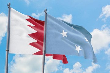 Fototapeta premium Micronesia and Bahrain flags waving in the wind against white cloudy blue sky together. Diplomacy concept, international relations.