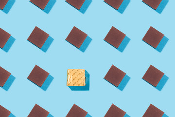 Chocolate slice pattern, concept, top view flat lay of pieces of chocolate with dark shadow one of them in candy wrappers on blue background