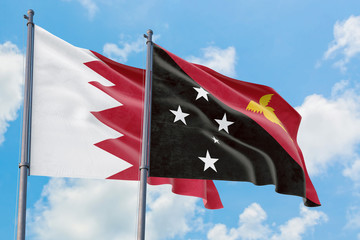Papua New Guinea and Bahrain flags waving in the wind against white cloudy blue sky together. Diplomacy concept, international relations.