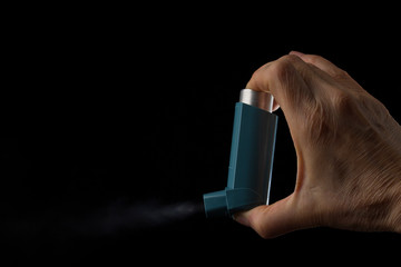 Hand holds inhaler for asthmatics on a black background - obrazy, fototapety, plakaty