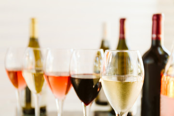 Wine tasting set in the light airy environment. Custom wine tasting concept. Glasses of wine and bottles on the glass table and light background.
