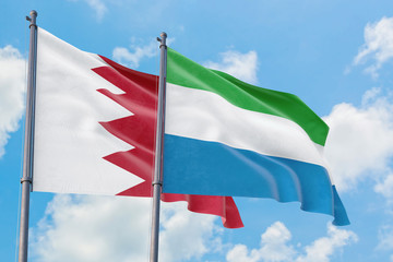 Fototapeta na wymiar Sierra Leone and Bahrain flags waving in the wind against white cloudy blue sky together. Diplomacy concept, international relations.