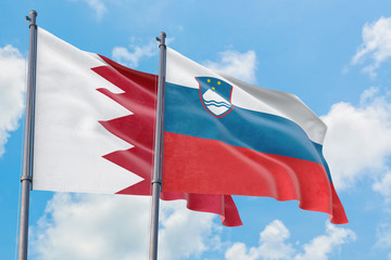 Slovenia and Bahrain flags waving in the wind against white cloudy blue sky together. Diplomacy concept, international relations.
