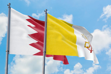 Vatican City and Bahrain flags waving in the wind against white cloudy blue sky together. Diplomacy concept, international relations.