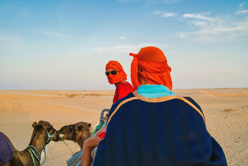 Tourists in the Sahara desert on camels. The entertainment of tourists. Camel caravan in the desert.
