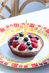 Birthday cake with a candle, with raspberries, blueberries and cream close-up, vertical