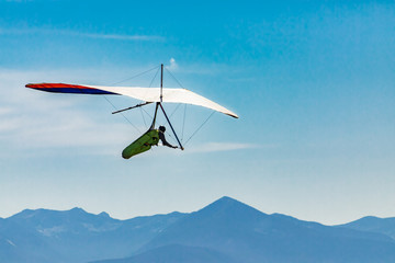 Fototapeta na wymiar Flying hang glider man in action. Beautiful mountains view in the background. Extreme leisure activities in Creston, British Columbia, Canada