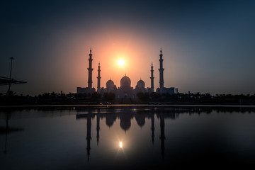 The Sheikh Zayed Grand Mosque with reflection on water and a beautiful golden hour sunset view