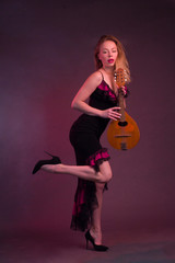 Blonde, in a black Spanish Dressdress flamenco dancer in action, with a mandolin in her hands on a Burgundy background of the Studio