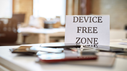 No tech allowed. Close up of mobile phones on the office table with device free zone sign