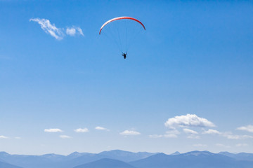 Fototapeta na wymiar Beautiful scene of flying paraglider over Kootenay valley mountains. Long shot of flying paraglider man. Recreational and competitive adventure sport