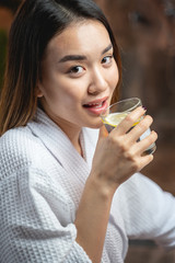 Cute charming Asian lady drinking tea after beauty procedures in salon