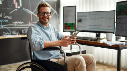 Successful trader. Portrait of young and cheerful male businessman in a wheelchair holding his...