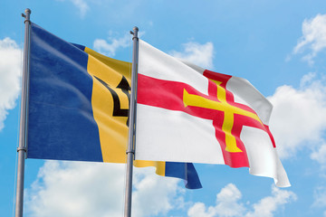 Guernsey and Barbados flags waving in the wind against white cloudy blue sky together. Diplomacy concept, international relations.