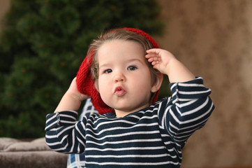 A child puts on a hat. A red hat and a child. shows a finger. The child is 0-1 years old. one year old child portrait.