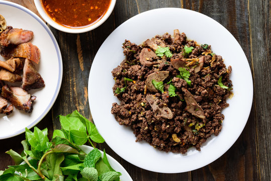 Northern Thai food, spicy minced pork salad (Larb Moo Kua) eating with grilled intestine and fresh vegetables on wooden background, top view