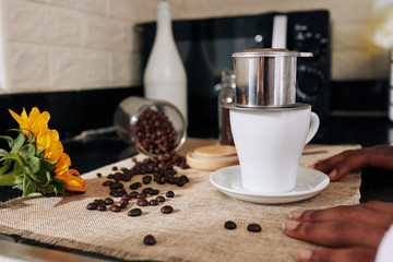 Porcelain mug and traditional Vietnamese coffee maker on kitchen table of young woman