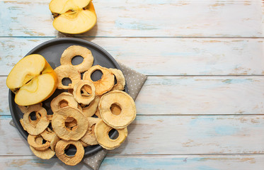Dried apple chips on a gray plate on a white wooden background. Diet snack with copy space. Top view
