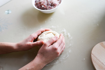 Fototapeta premium Dough with minced meat. Hands wrinkle the dough closeup. Manual preparation of the test. Homemade baking. Cooking dumplings and pasties.