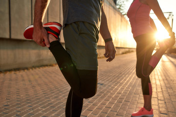 Warming up. Cropped photo of fitness couple in sports clothing doing stretching exercises before running while standing outdoors