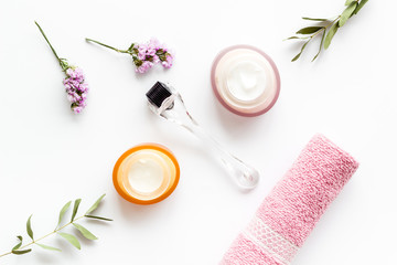 Cosmetologist tools. Dermaroller, creams near leaves and flowers on white background top-down flat...