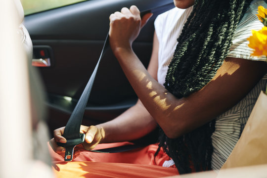 Cropped image of young woman fastening seat belt in taxi car