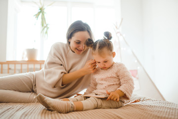 Cheerful mother and her daughter little daughter watching cartoons on phone lying In bed at home. Happy loving family. Modern wireless tech usage free time concept. Bedtime Fun.