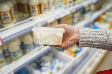 Female hand holding cottage cheese in plastic packaging in the supermarket