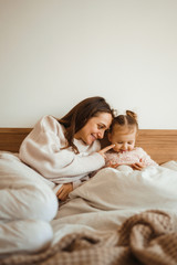 Cheerful mother and her daughter little daughter watching cartoons on phone lying In bed at home. Happy loving family. Modern wireless tech usage free time concept. Bedtime Fun.